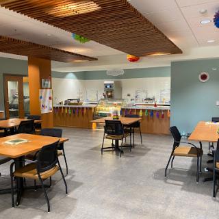 A spacious dining area with wooden tables and chairs, ready for guests, featuring a buffet setup in the background.