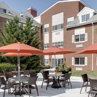 A sunny patio with tables and orange umbrellas in front of a brick building.