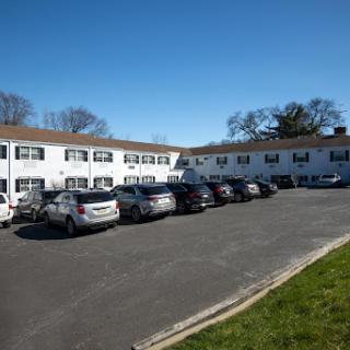 A view of a residential building with a parking lot filled with cars under a clear blue sky.