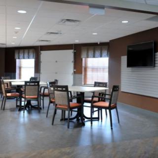 A modern dining area with tables and chairs, featuring a wall-mounted television and large windows.