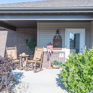 A cozy front porch with rocking chairs and greenery on a sunny day.