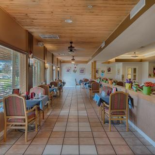 A cozy restaurant dining area with neatly arranged tables and chairs, ambient lighting, and a wooden ceiling.
