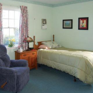 A cozy bedroom with a single bed, armchair, and wooden nightstand by the window.