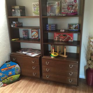A pair of wooden bookshelves filled with toys and games, offering a tidy storage solution in the corner of a room.