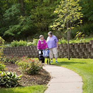 Two elderly individuals walking on a pathway surrounded by greenery.