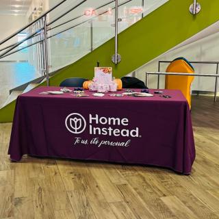 A promotional table set up by Home Instead, featuring brochures and materials for an event.