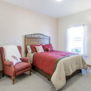 A cozy bedroom with red bedding and an armchair next to a window.