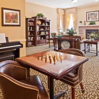 A cozy living room with a chess table, piano, fireplace, and bookshelves.
