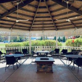 A cozy outdoor gazebo with seating and a central fire pit, surrounded by lush greenery.