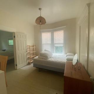 A simple bedroom with a bed, chest of drawers, and shelves by the window.