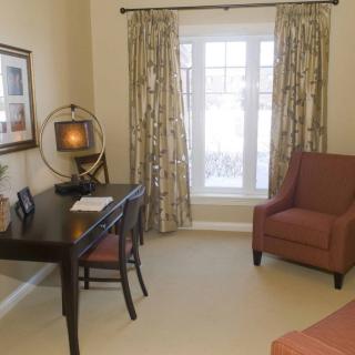 A cozy home office featuring a desk, chair, and window with curtains.