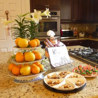 A kitchen scene with a tiered fruit stand of oranges, decorated cookies on plates, and a luxurious granite island countertop.