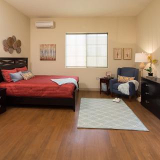 A cozy bedroom with red bedding, wooden flooring, and a comfortable armchair by the window.