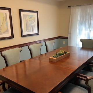 A dining room featuring a large wooden table surrounded by chairs, with framed artwork on the walls and a decorative centerpiece.
