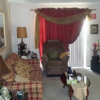 A cozy living room with plaid sofa, armchair, and red curtains.