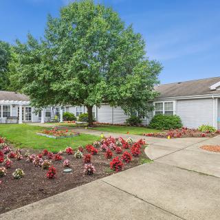 A charming house with a beautifully landscaped garden featuring colorful flowers and a large tree, set alongside a winding pathway.