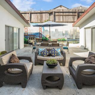 A cozy outdoor patio area featuring comfortable seating, a dining table under an umbrella, and decorative plants.