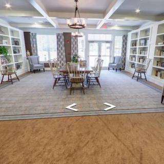 A spacious and elegant room with bookshelves, a dining table, and chairs, featuring large windows and soft lighting.