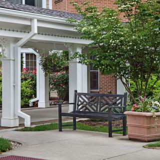 An outdoor bench situated by a garden under a covered walkway next to a brick building.