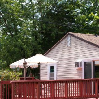 A cozy house with a wooden deck and an outdoor umbrella surrounded by lush trees.