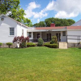 A quaint white house with a spacious green lawn and well-maintained garden under a partly cloudy sky.