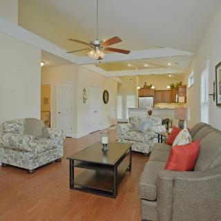 A spacious living room with an open floor plan connecting to the kitchen, featuring comfortable sofas, a coffee table, and a ceiling fan.