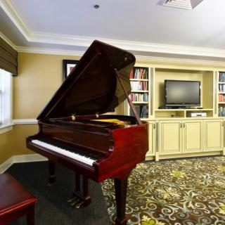 A cozy living room featuring a grand piano with a bookshelf and television nearby.