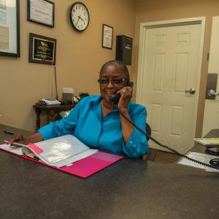 A woman in an office speaking on the phone with files on her desk.