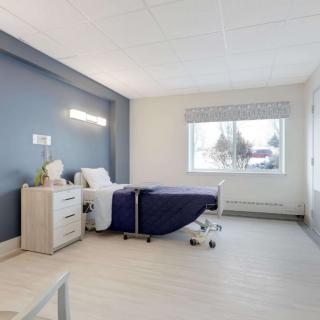 A clean and minimalist hospital room with a single bed and a large window.