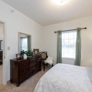 A cozy bedroom featuring a wooden dresser, a large mirror, and a bed with white linens.