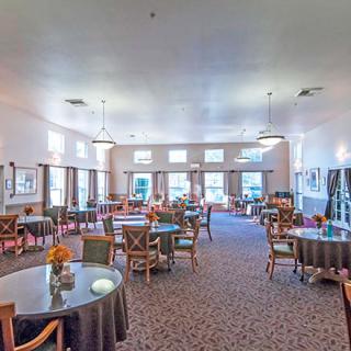 A spacious dining room with multiple tables and chairs, well-lit by natural and artificial lighting.
