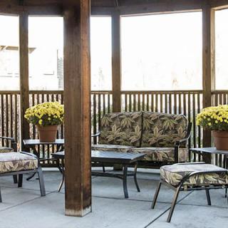 A cozy patio setup with cushioned outdoor furniture and potted yellow flowers under a wooden gazebo.