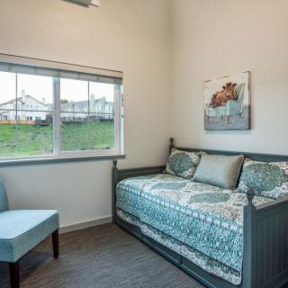 A cozy bedroom with a daybed and a chair, featuring a large window and artwork on the wall.