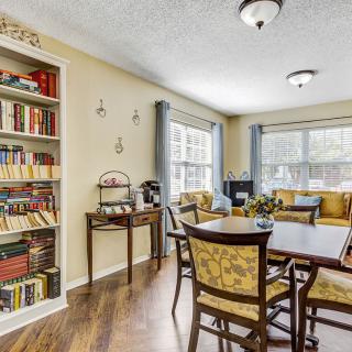 A well-lit living room with a dining area and a large bookshelf, featuring comfortable seating and wooden flooring.