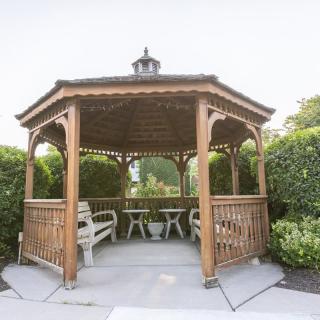 A wooden gazebo surrounded by greenery, featuring benches and tables inside.