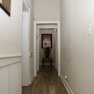 A narrow hallway with wood flooring and white walls, featuring doorways leading to other rooms.