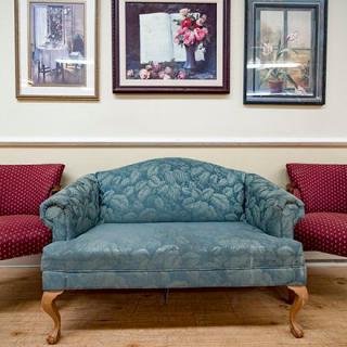 A vintage-style blue sofa flanked by two red chairs, set beneath framed artwork in a cozy living room.