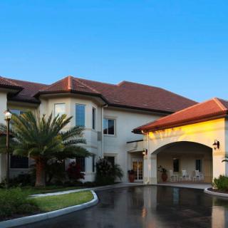 A modern building with a red-tiled roof and palm tree landscaping, featuring an inviting entrance and driveway.