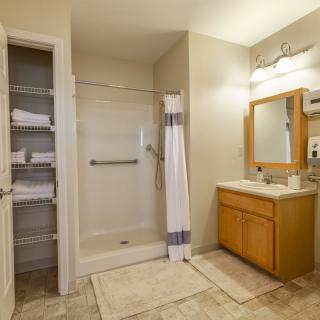 A well-organized bathroom featuring a shower, vanity with mirror, and neatly stacked towels.