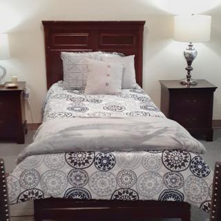 A cozy bedroom with a single bed, flanked by nightstands and lamps, featuring decorative bedding.