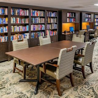 A cozy library reading area with a large table, surrounded by bookshelves filled with books.