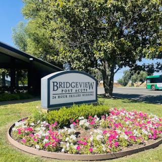 Sign for Bridgeview with colorful flowers and trees in the background.