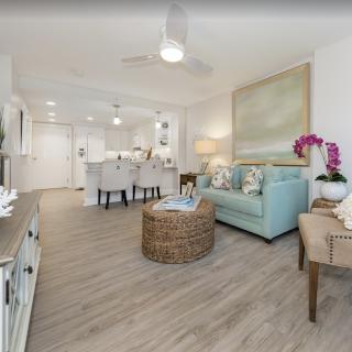 A modern living room with an open floor plan, featuring pastel-colored furnishings and wood flooring.