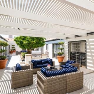 A modern patio area with comfortable seating under a pergola, featuring potted plants and a stylish outdoor setting.