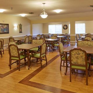 An empty dining room with wooden flooring and elegantly arranged tables and chairs.