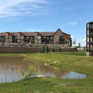 A picturesque residential complex set against a serene pond under a clear blue sky.