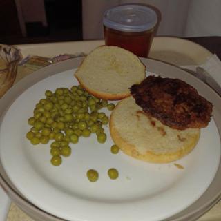 A plate with a burger on a bun served with peas, accompanied by a drink.