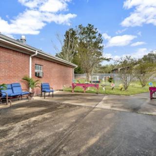 A spacious outdoor patio area with benches and chairs next to a brick building, surrounded by a garden and trees.
