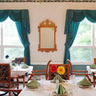 An elegantly decorated dining area with set tables, teal curtains, and a decorative mirror on the wall.