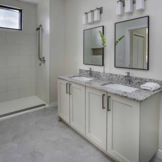 A modern bathroom featuring a double sink vanity with granite countertops and a spacious walk-in shower.